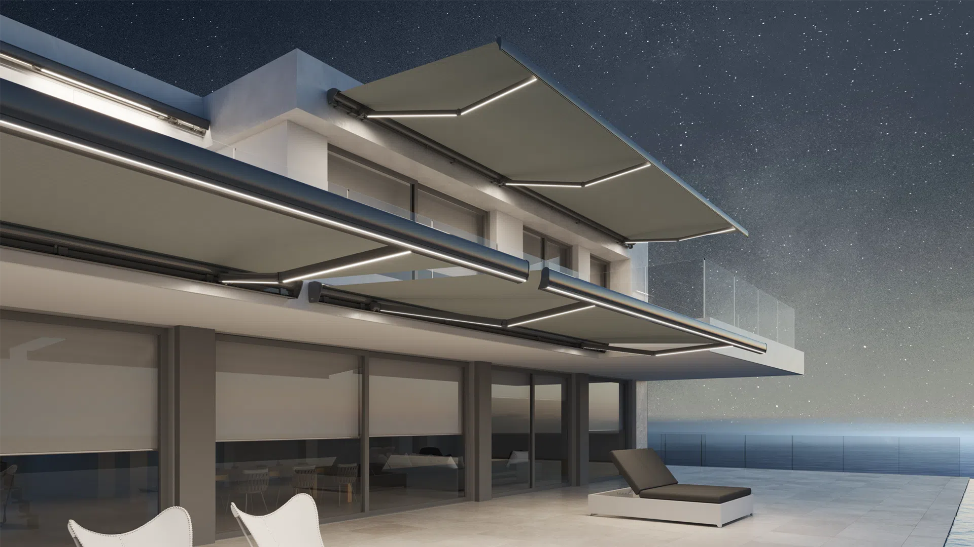 Night view of a modern apartment balcony with outdoor seating and glass sliding doors, overlooking the ocean under a starry sky.