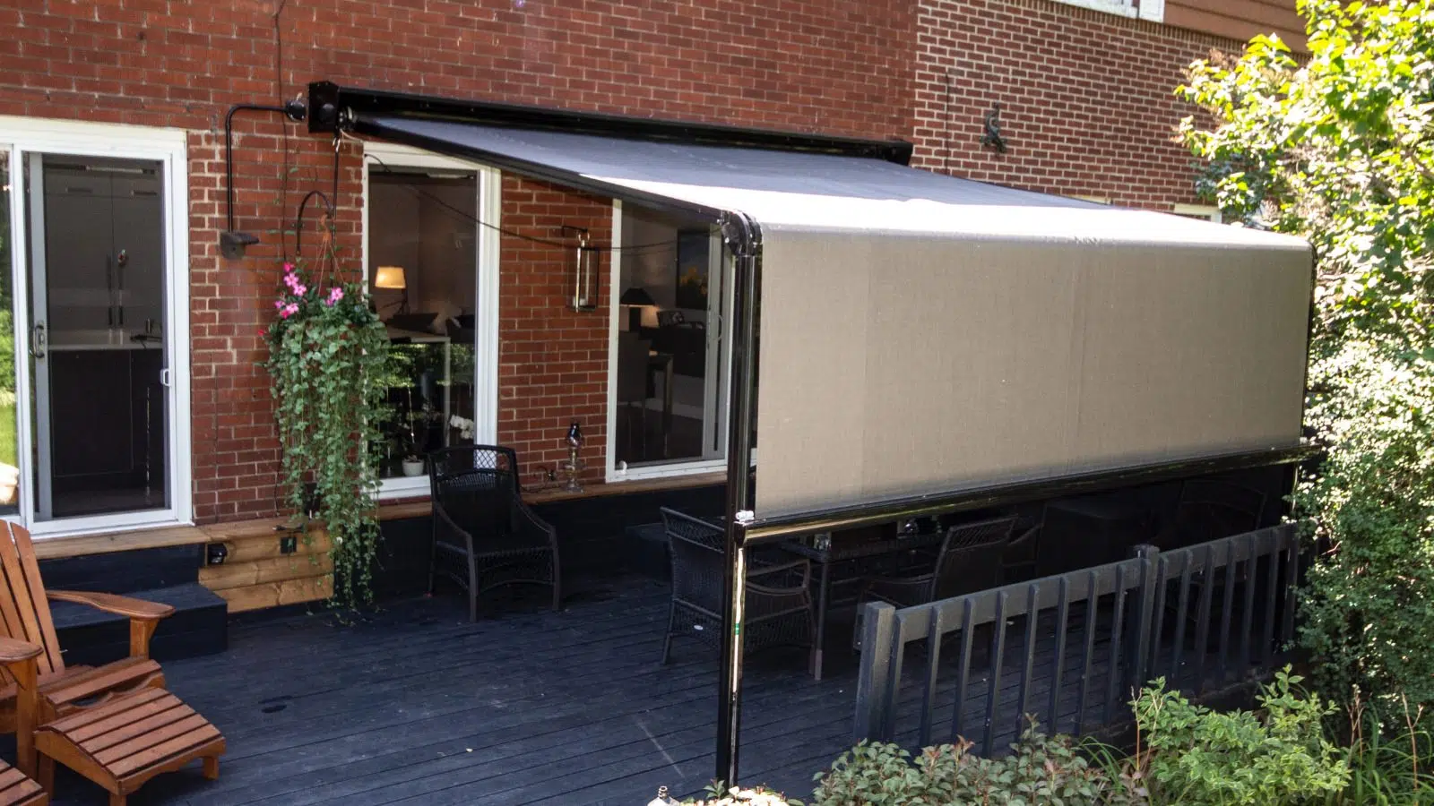 A backyard patio with a covered pergola attached to a brick house, black outdoor furniture, and lush greenery.