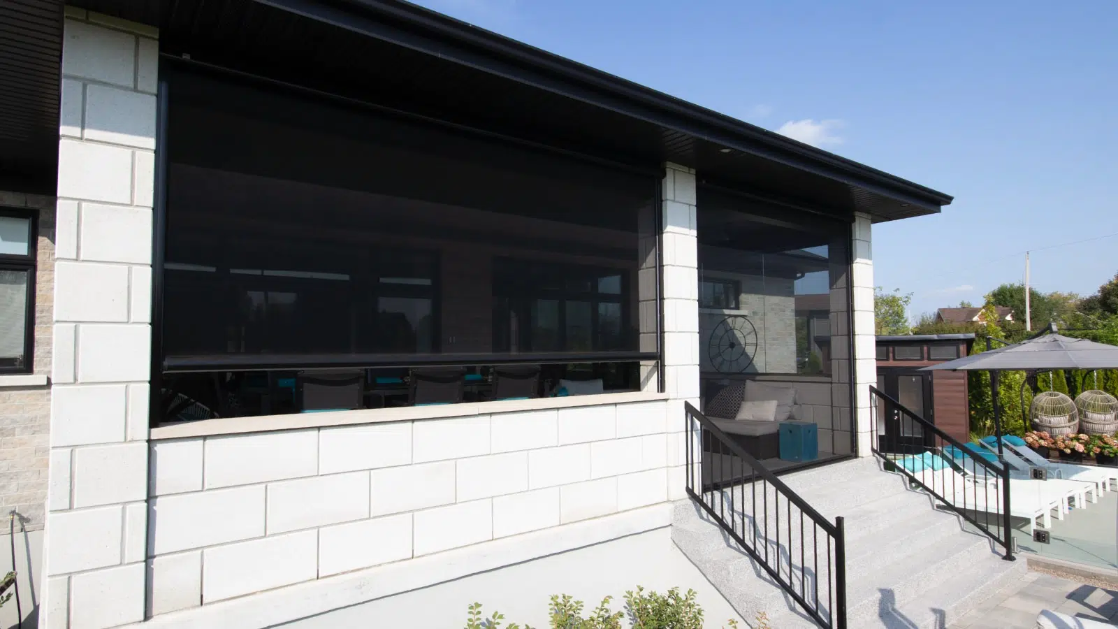 Modern house with a screened porch, outdoor seating, and a pool area with lounge chairs and umbrellas.