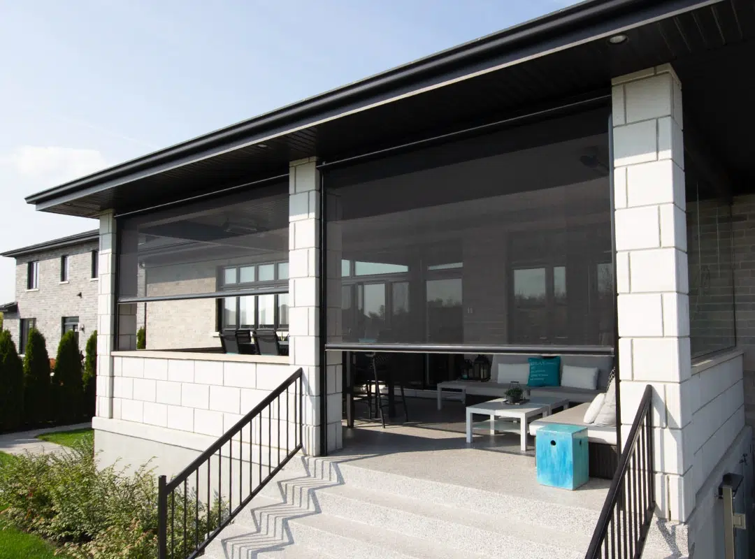 A house with a porch that has screened-in sides, white brick pillars, black railings, and outdoor furniture, including a white table, chairs, and a blue side table.