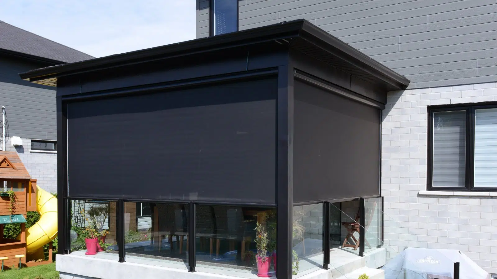 A modern house with grey siding, white brick walls, and a black screened-in porch with glass railings and pink flower pots outside.
