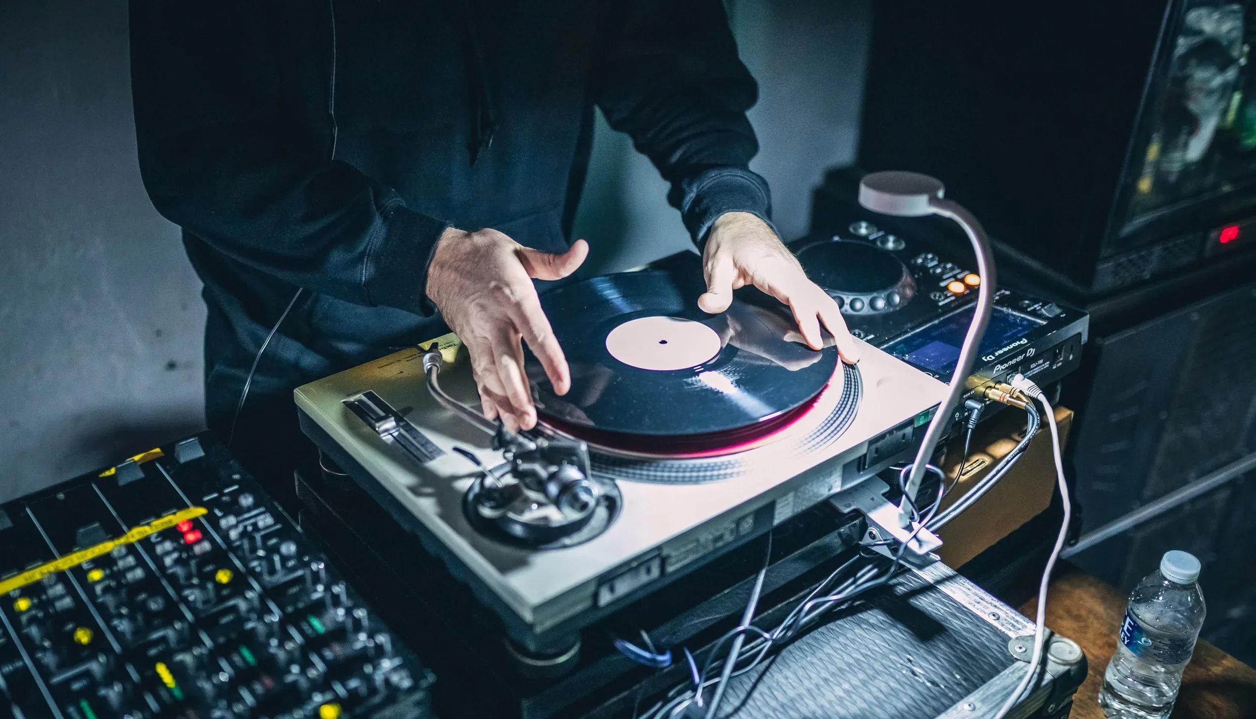 DJ with turntable and mixing equipment playing music in a dark setting.