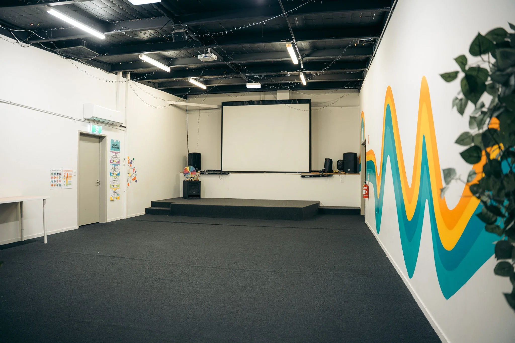 Empty indoor stage area with a large projection screen, black speakers, and colourful wall art on the Sunshine Coast. 