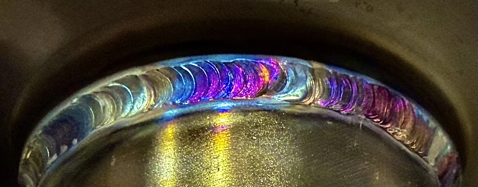 Close-up of a colorful rainbow pattern inside a metallic object, possibly a glass or a lens, with a reflective surface and vibrant light reflections.