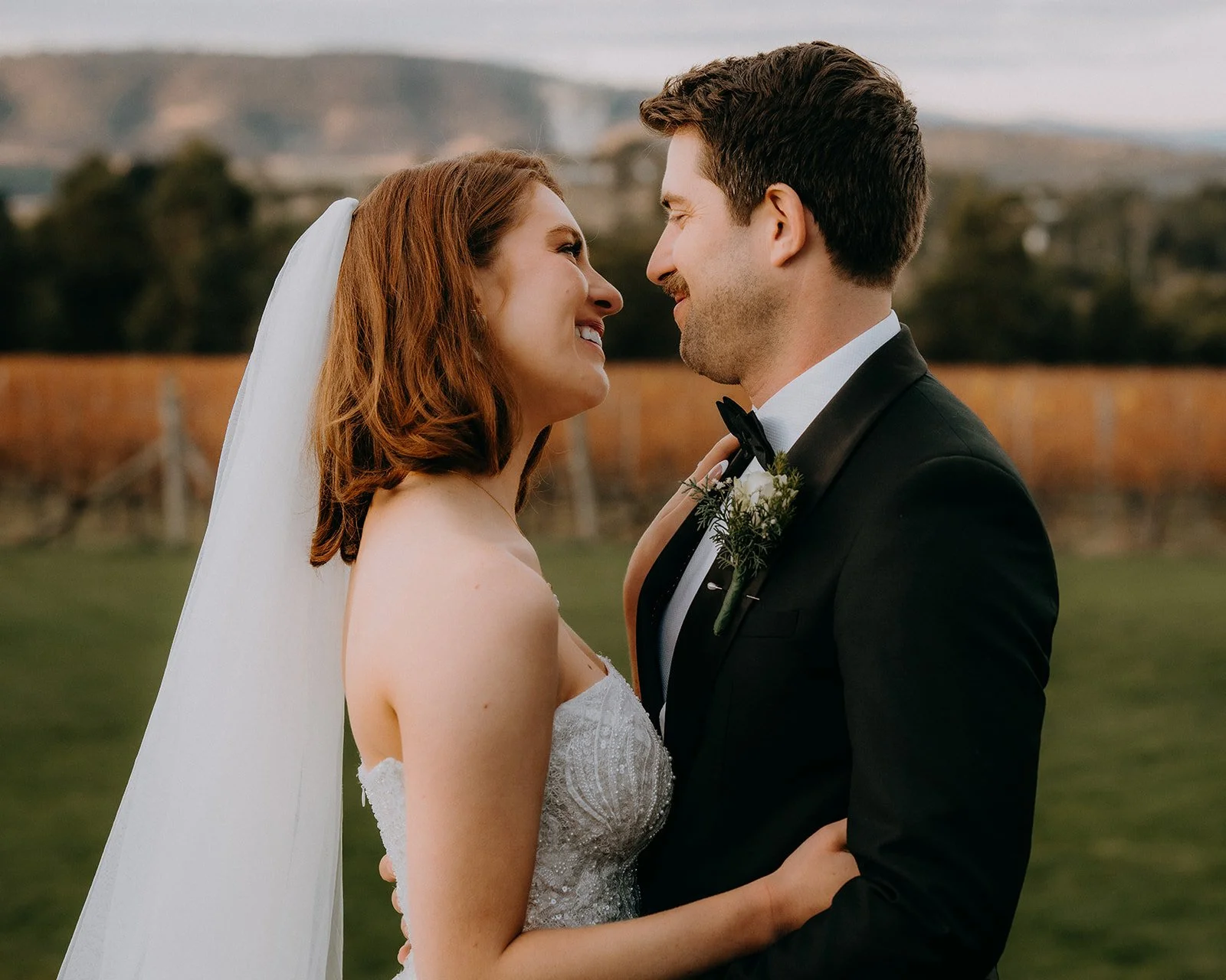 A bride and groom smiling at each other during their wedding outdoors.