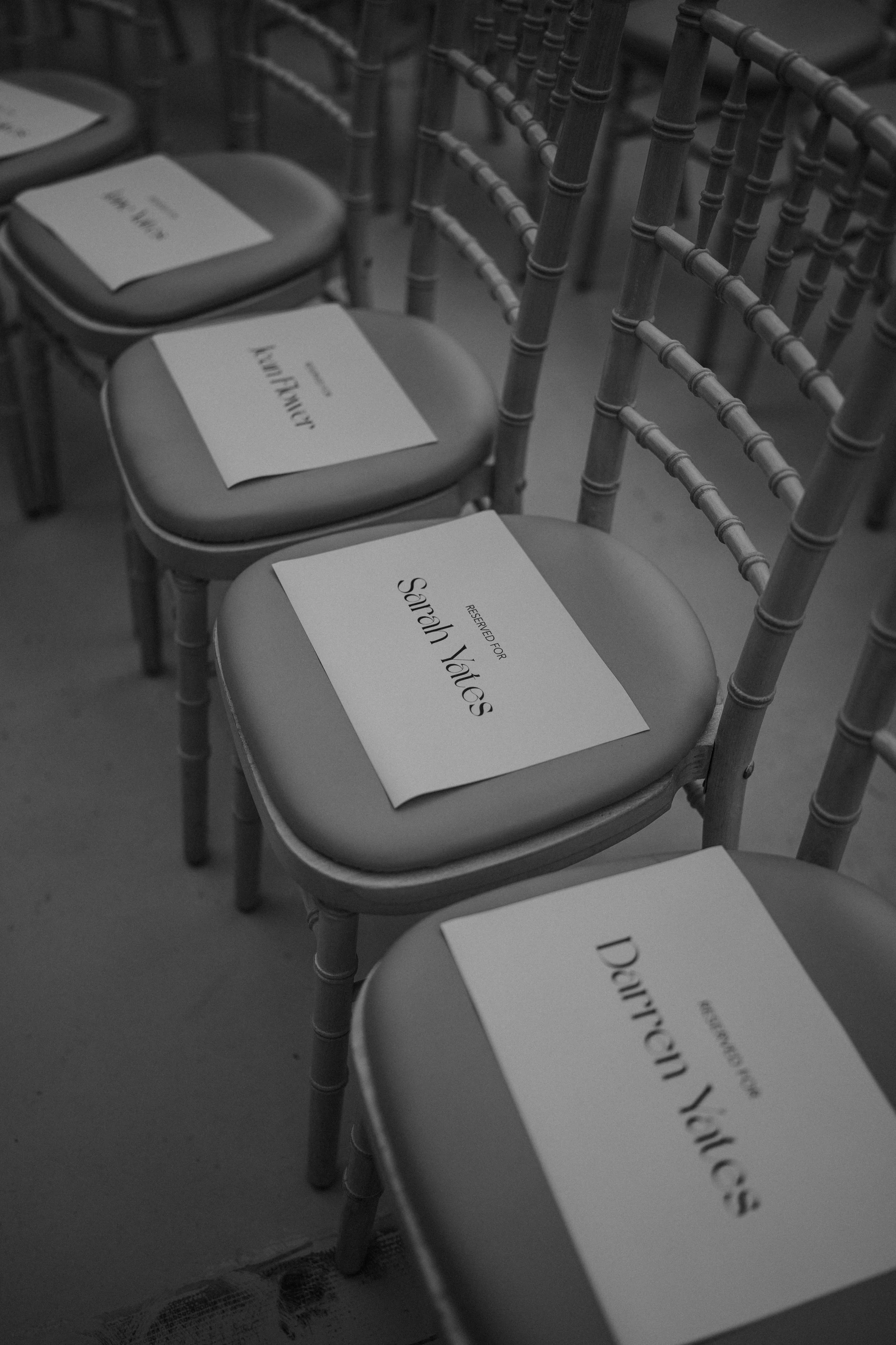 Multiple chairs with reserved tags placed on the seats, arranged in a row at a wedding.