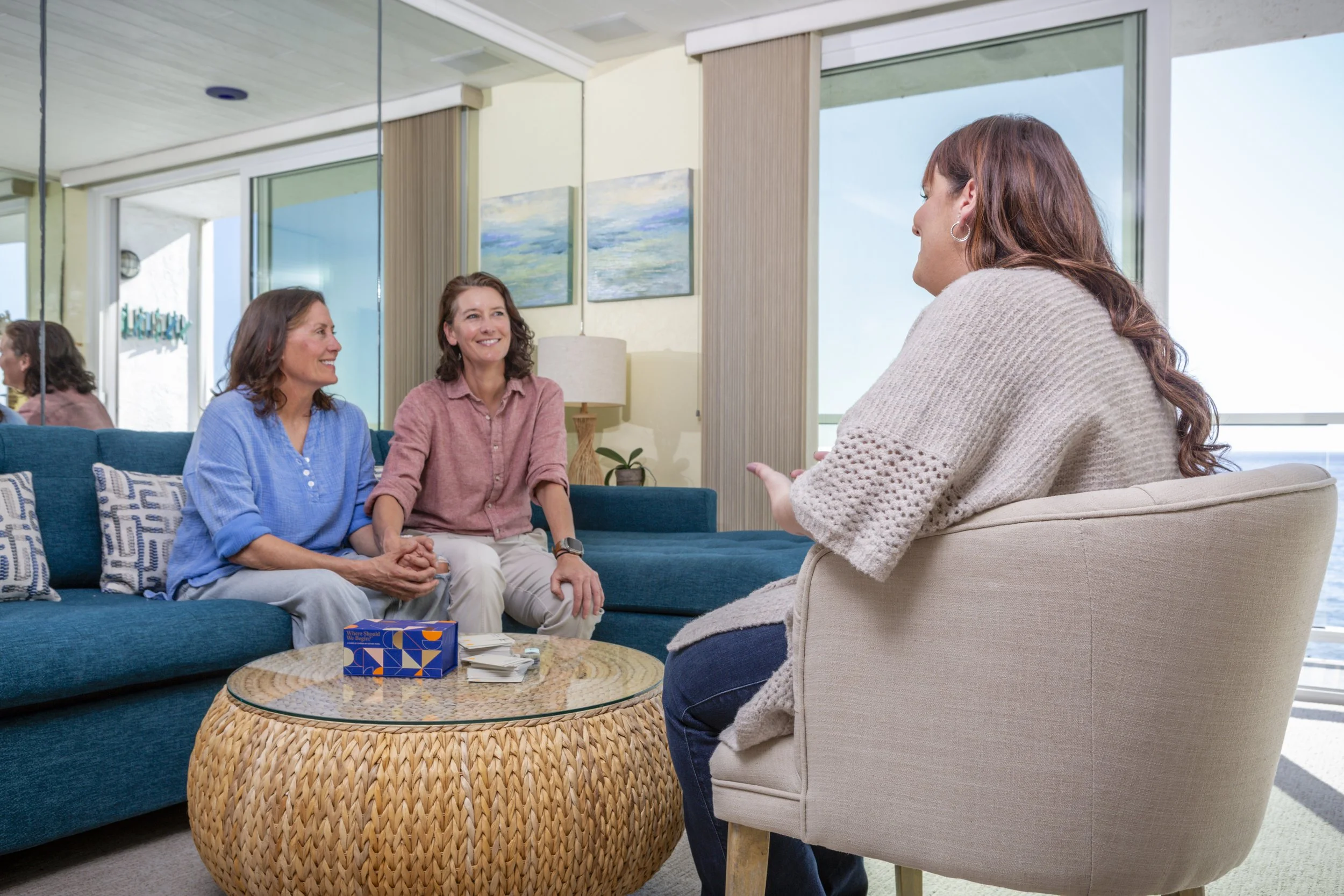 In a living room, three women, one a relationship coach, sit on a couch, discussing topics of personal growth and connection.