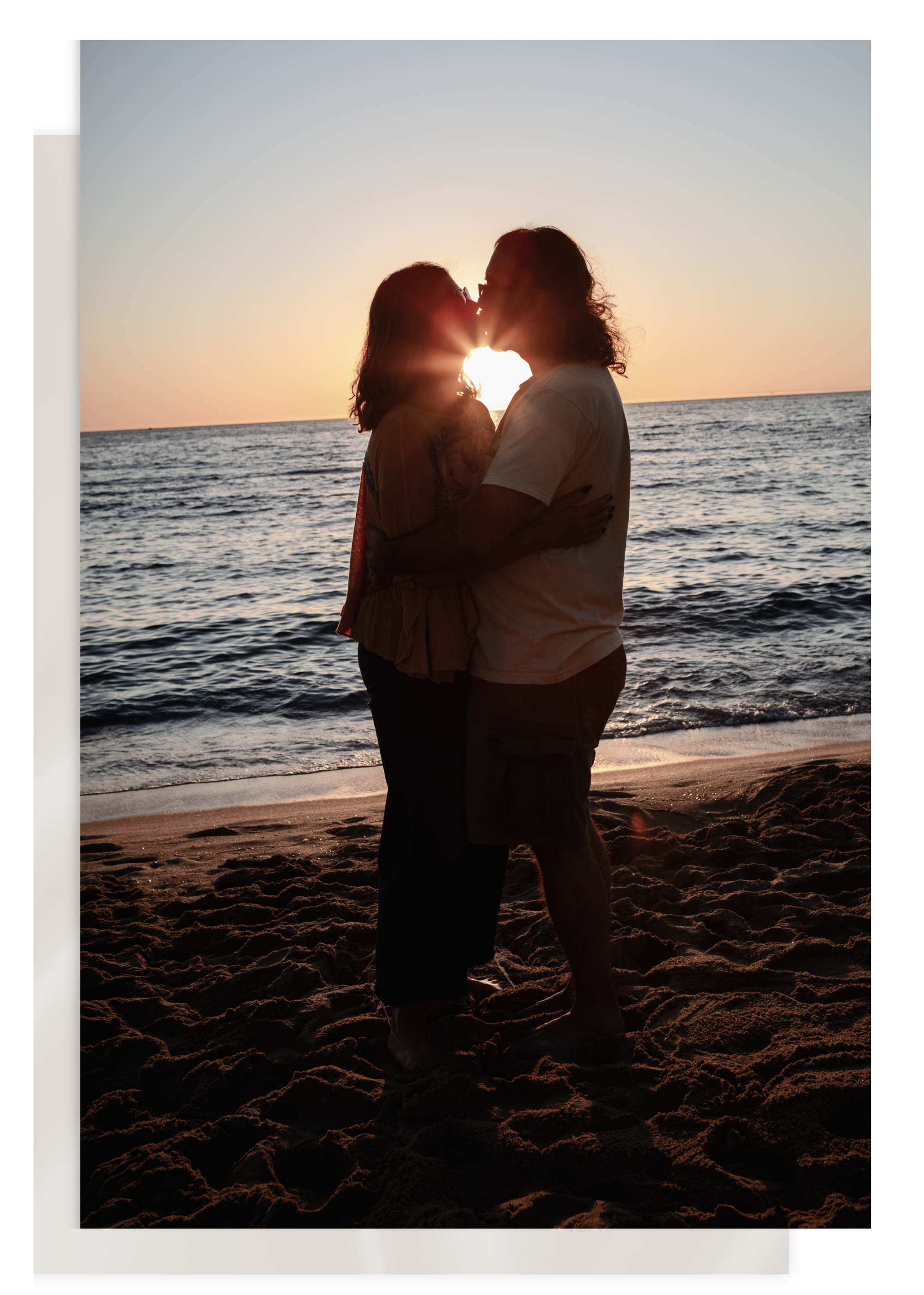 A couple standing on a sandy beach at sunset, kissing with the ocean in the background at a marriage retreat.
