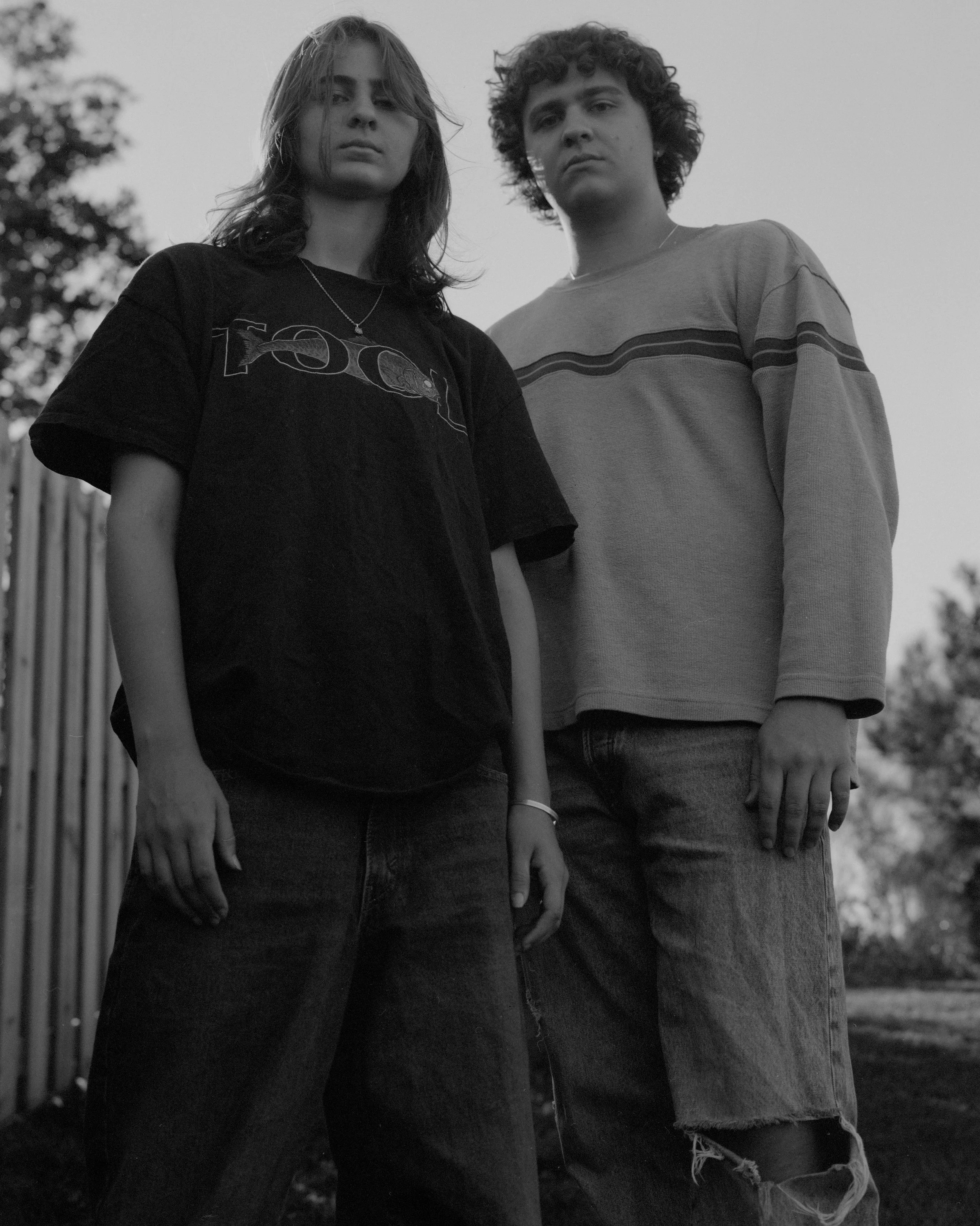 A black and white photo of a young woman and man standing outdoors, looking at the camera.
