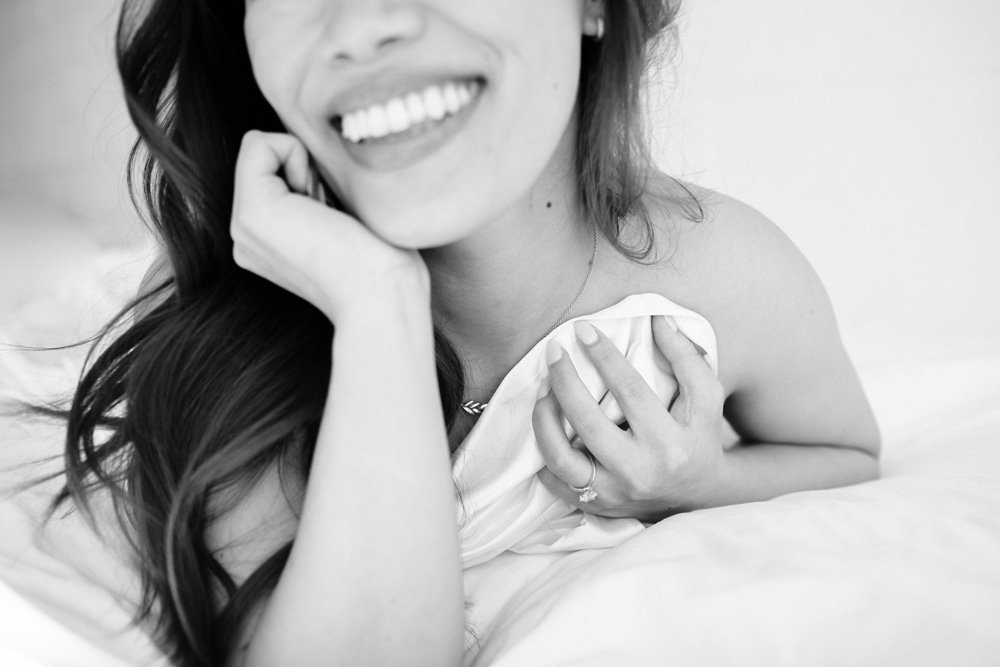 Boudoir client lying on her stomach and playfully pulling the sheets around herself