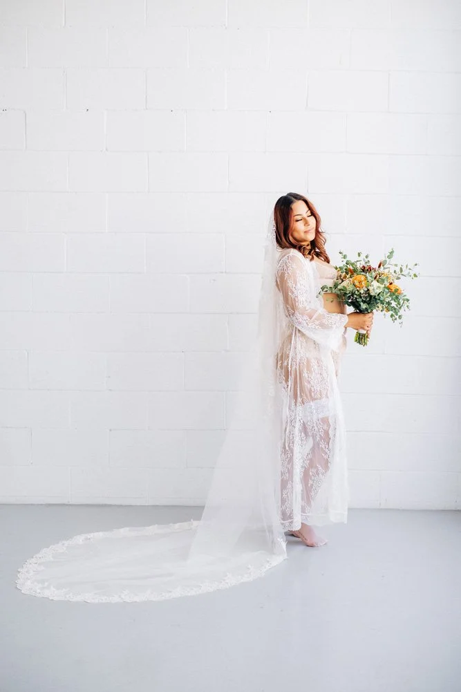 Bridal boudoir portrait in a sheer white blouse while holding a flower bouquet