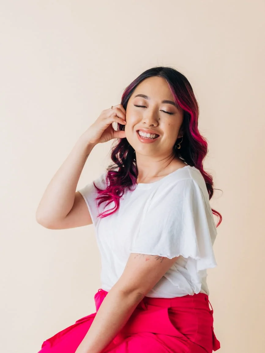 Debs, the photographer behind Hey Lovely Boudoir by Deb, smiling in pink pants and a white shirt