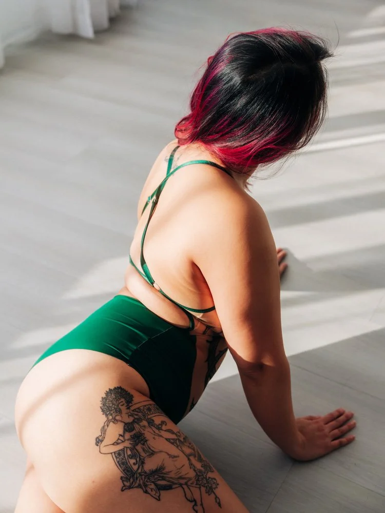 Boudoir portrait from behind while posing on the floor in a green bodysuit