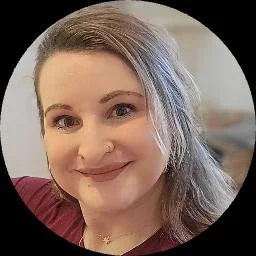 Close-up of a woman with light brown hair and a nose piercing, smiling
