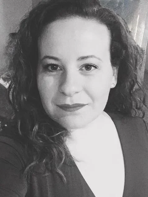 A woman with curly hair and a confident expression, wearing a dark top, in a black-and-white photograph.
