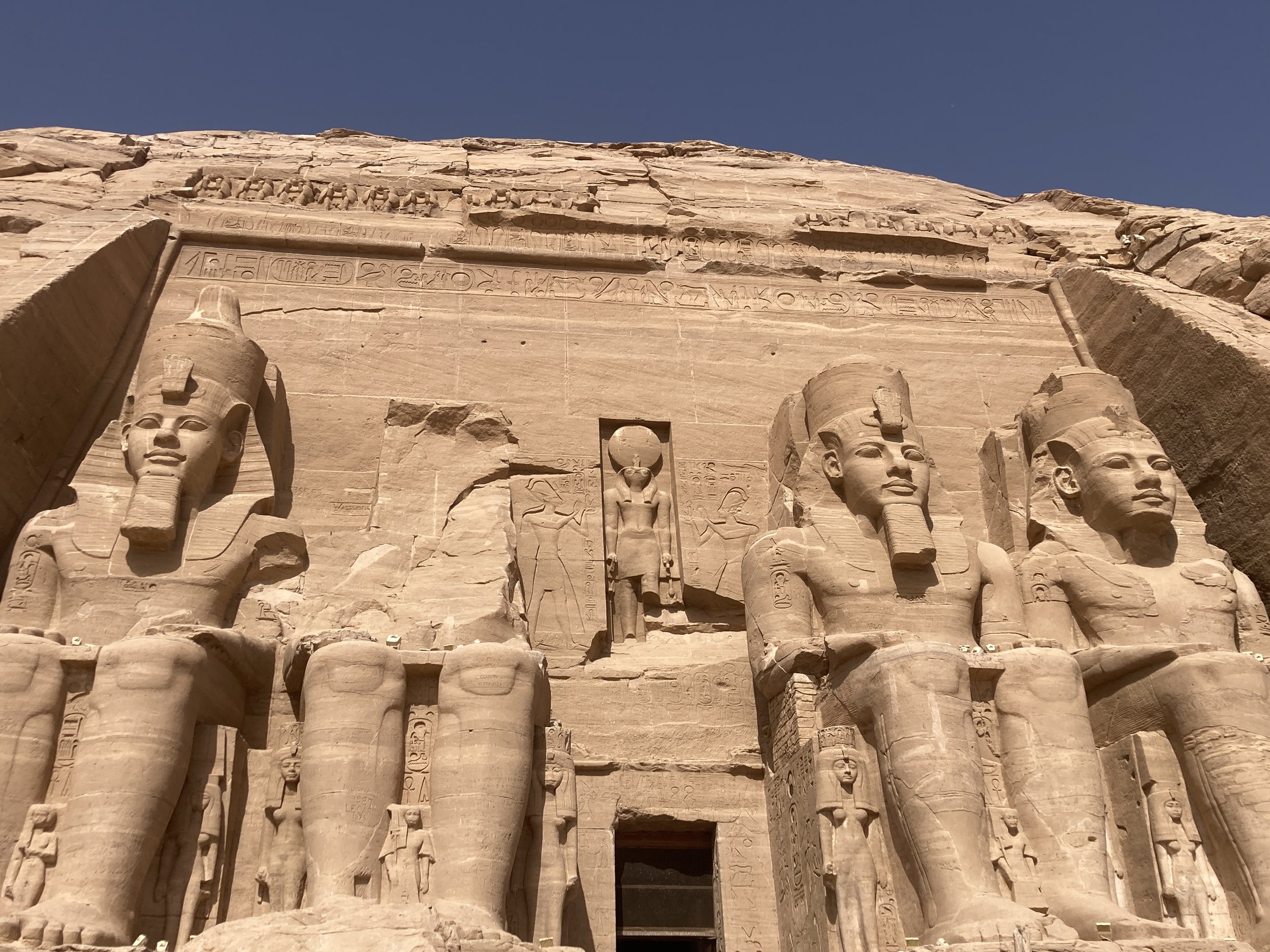 Close-up of the Great Temple of Abu Simbel, Egypt, featuring four colossal seated statues of Pharaoh Ramses II carved into the sandstone cliff, with hieroglyphics inscribed above.