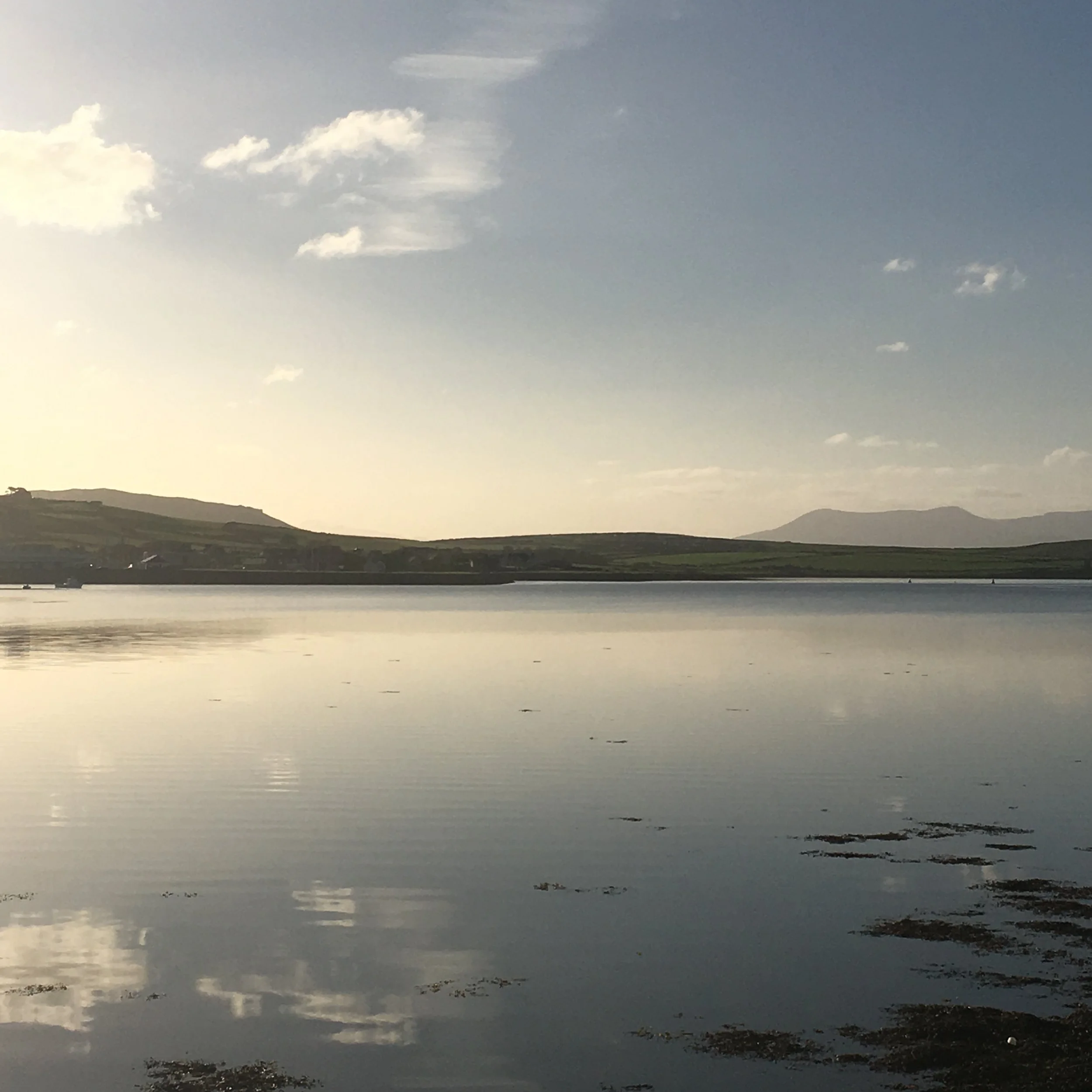 Dingle Harbour reflecting the sky and distant mountains with a partly cloudy sky overhead.