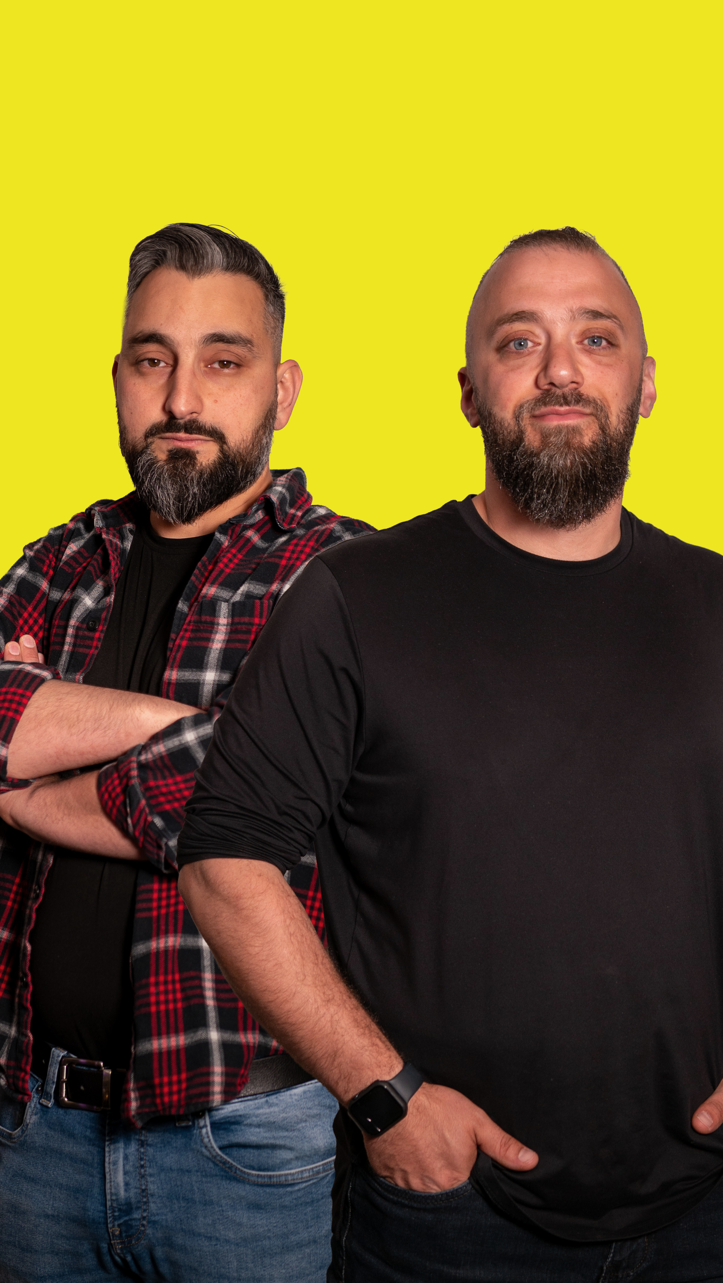 Two men standing with arms crossed in front of a bright yellow background.