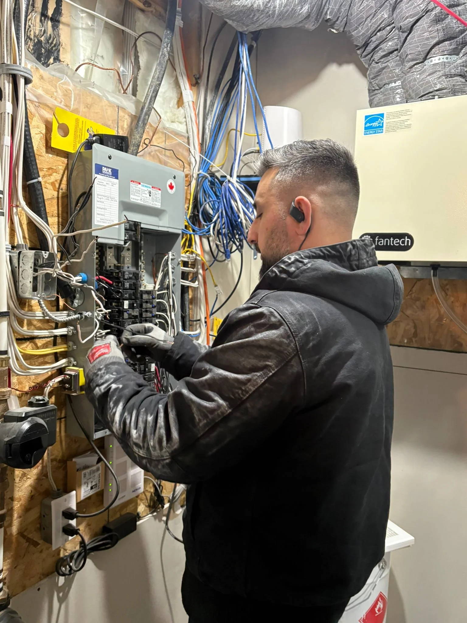 A technician working on an electrical panel with multiple wires and switches in an indoor setting.