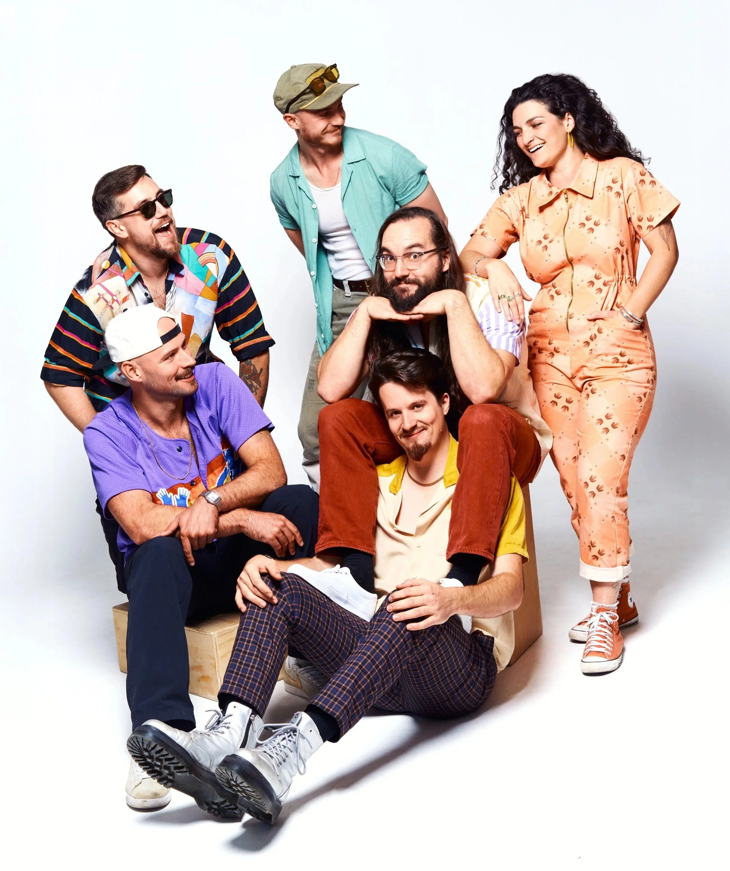 A candid shot of the band in colourful outfits at recent photoshoot in a studio. Bright colours, funky patterns, warm hues.