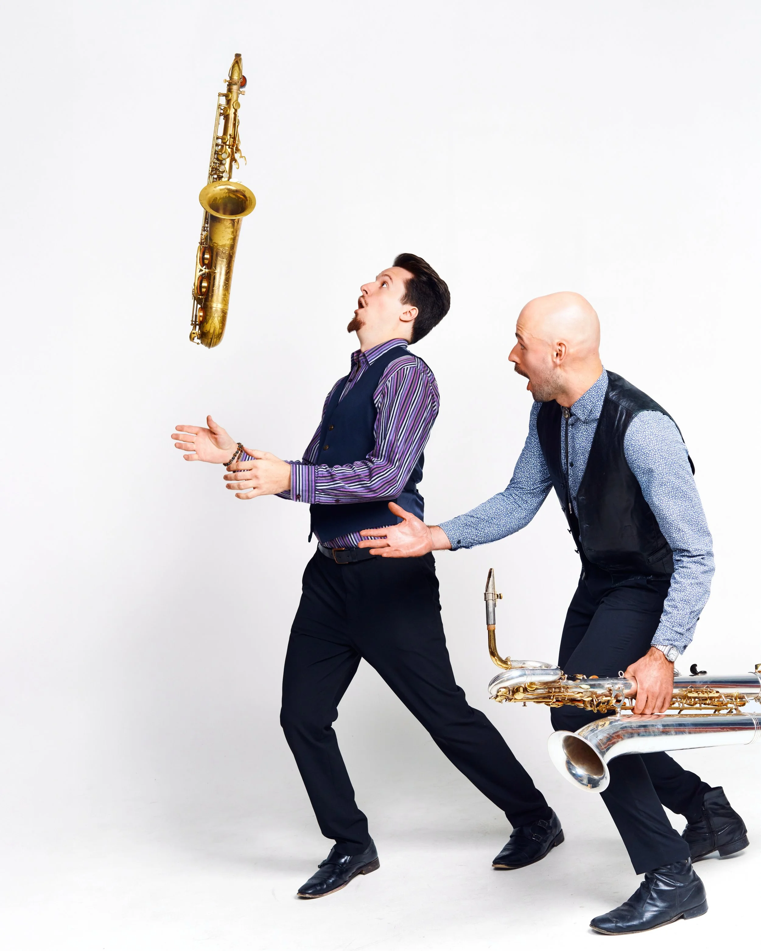 A playful photo of one saxophone player wating another throw his insturment in the air.