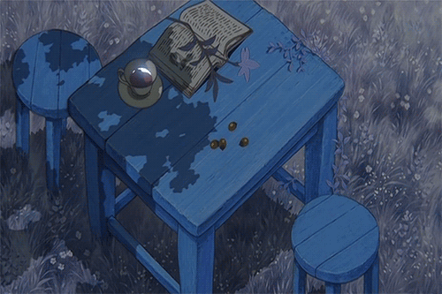 A blue table with a book, a crystal ball, and some coins on it, surrounded by a matching blue stool and grass with small white flowers.
