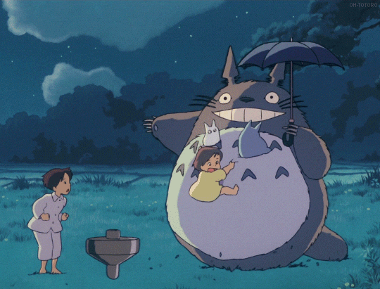 Animated scene with a large, friendly, dark gray creature holding a girl and an umbrella, and a young girl standing nearby in a grassy area at night.