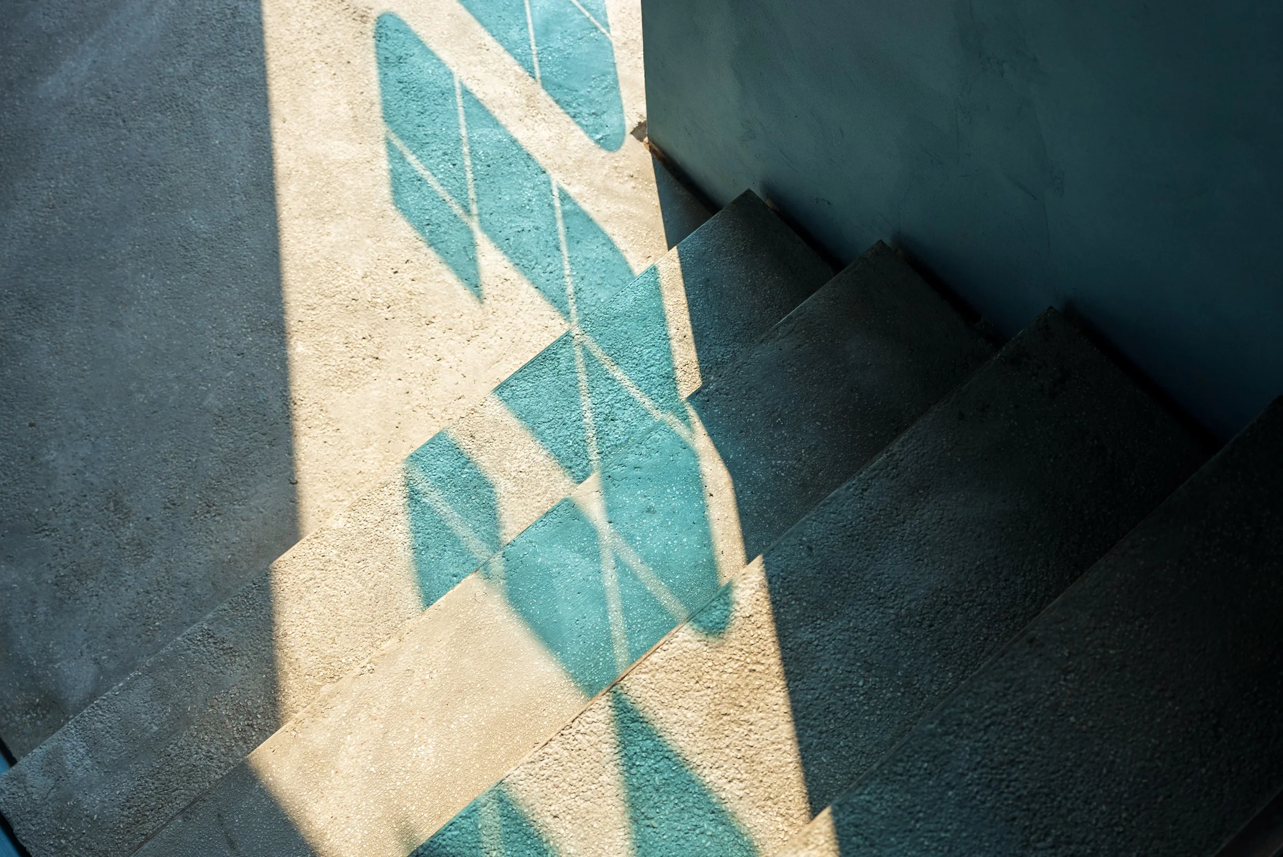 Sunlit concrete stairs with blue painted railings, shadow cast of a grid pattern on the ground.