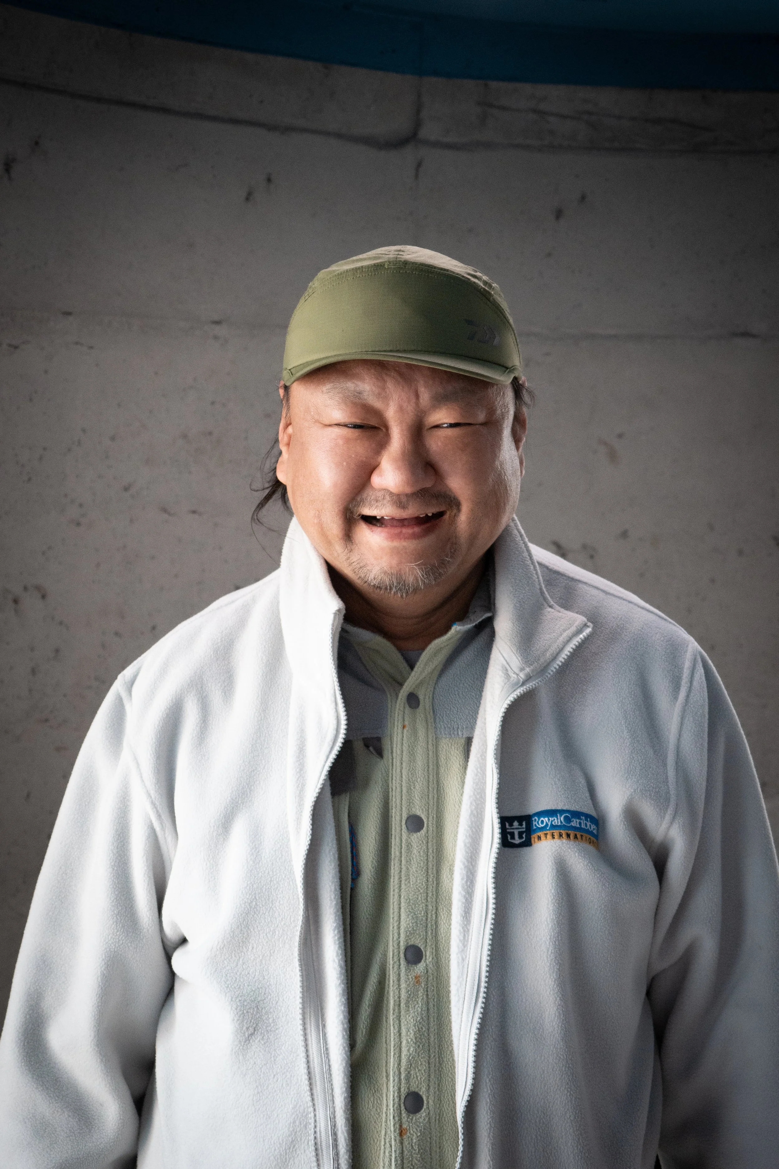 A man smiling and wearing a baseball cap, a fleece jacket, and a shirt with a "Royal Caribbean International" logo.