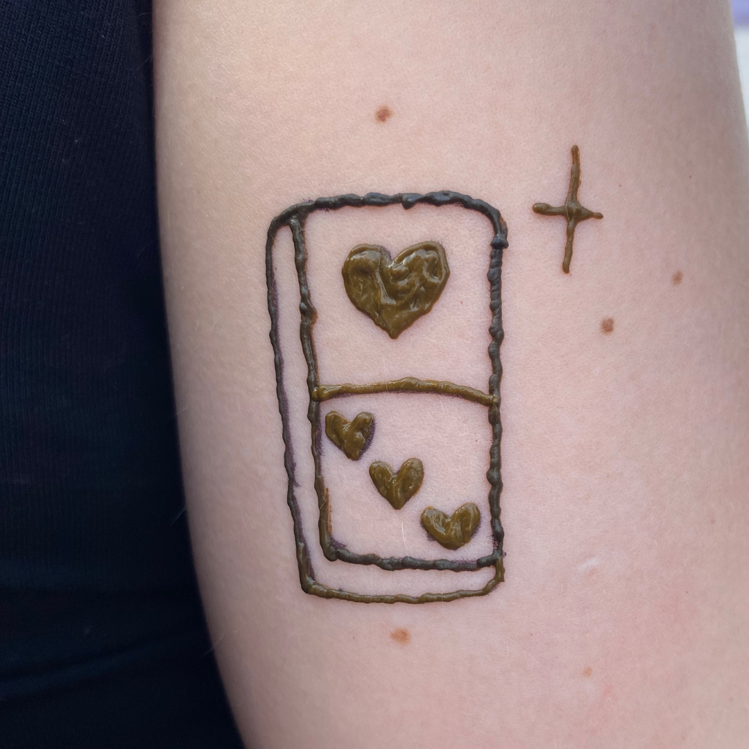Temporary tattoo of a refrigerator with four hearts inside it, one large heart at the top and three smaller hearts below, a cross symbol nearby.