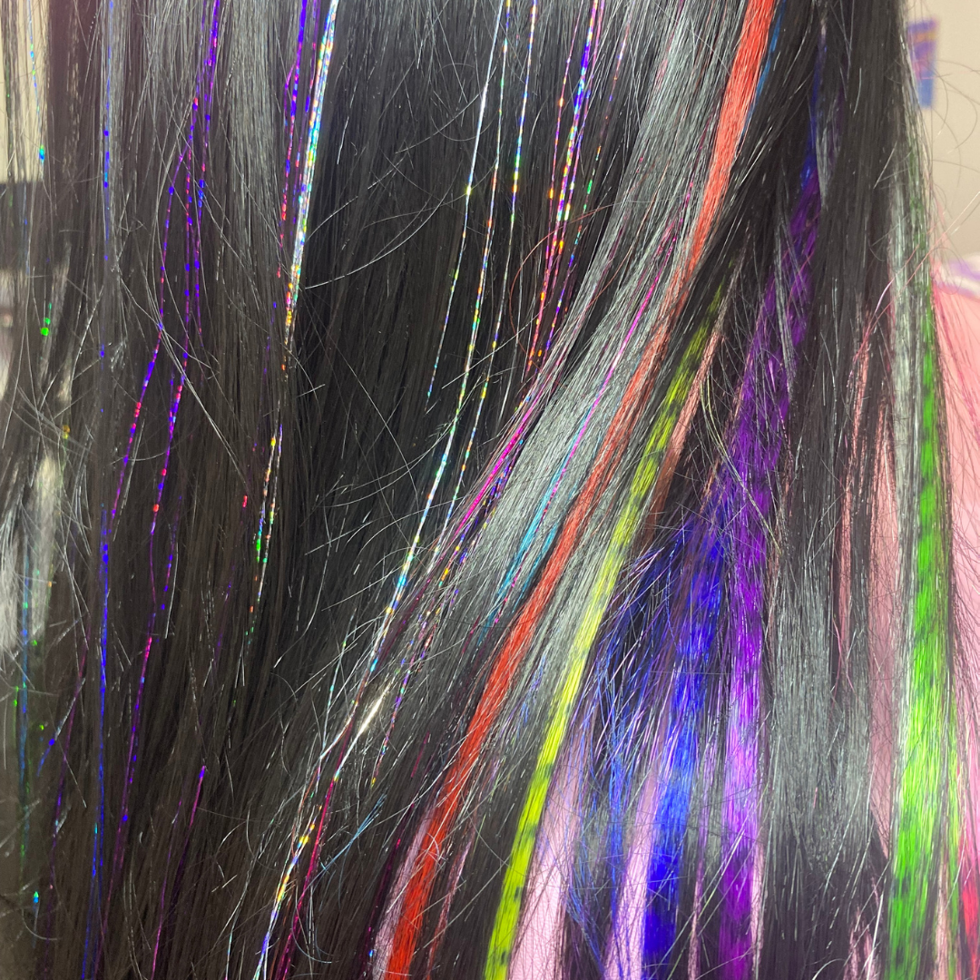 Close-up of black hair with colorful streaks and glitter.