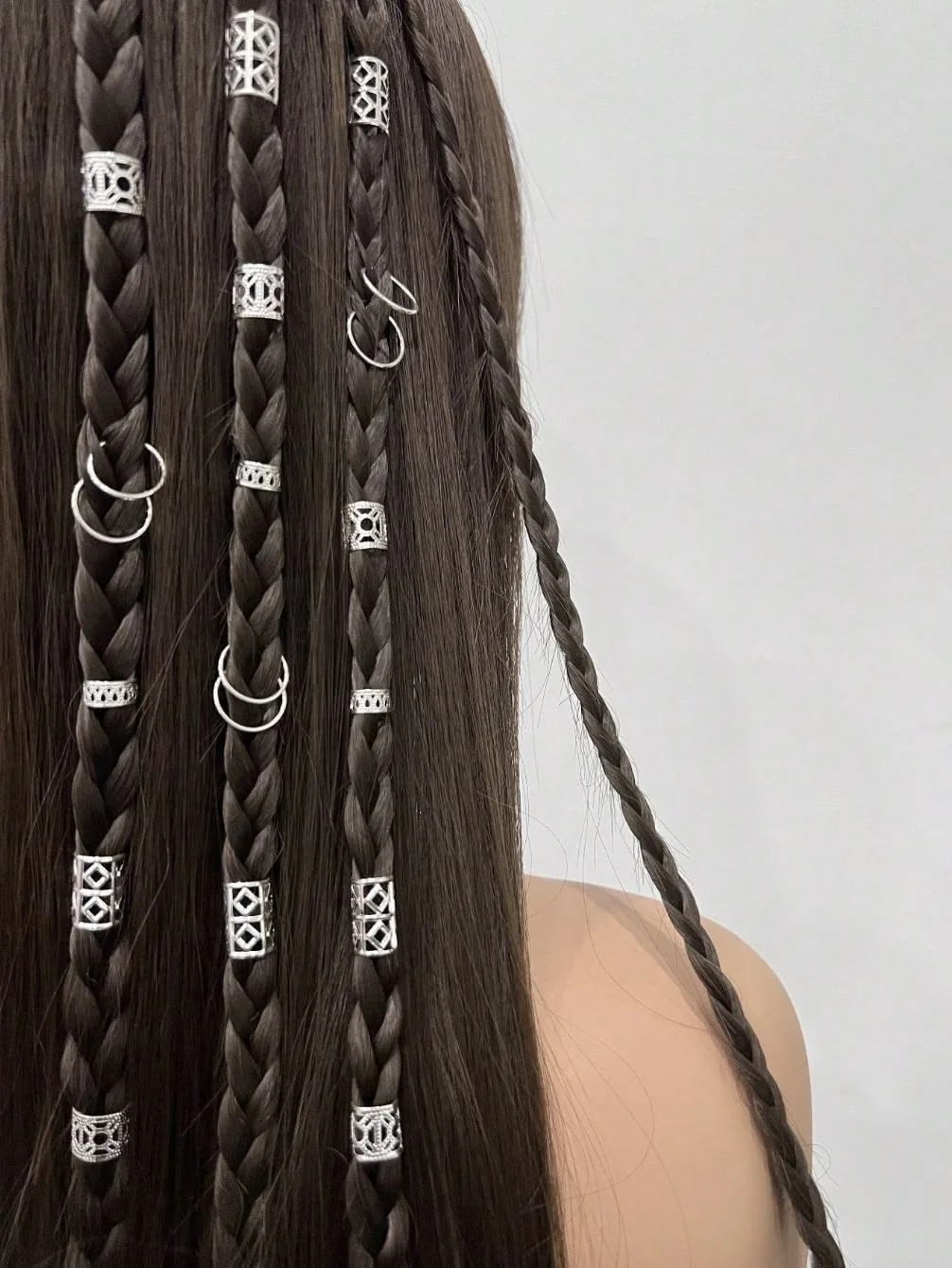 Close-up of a person with long, straight brown hair styled with multiple small braids, some adorned with silver hair rings.