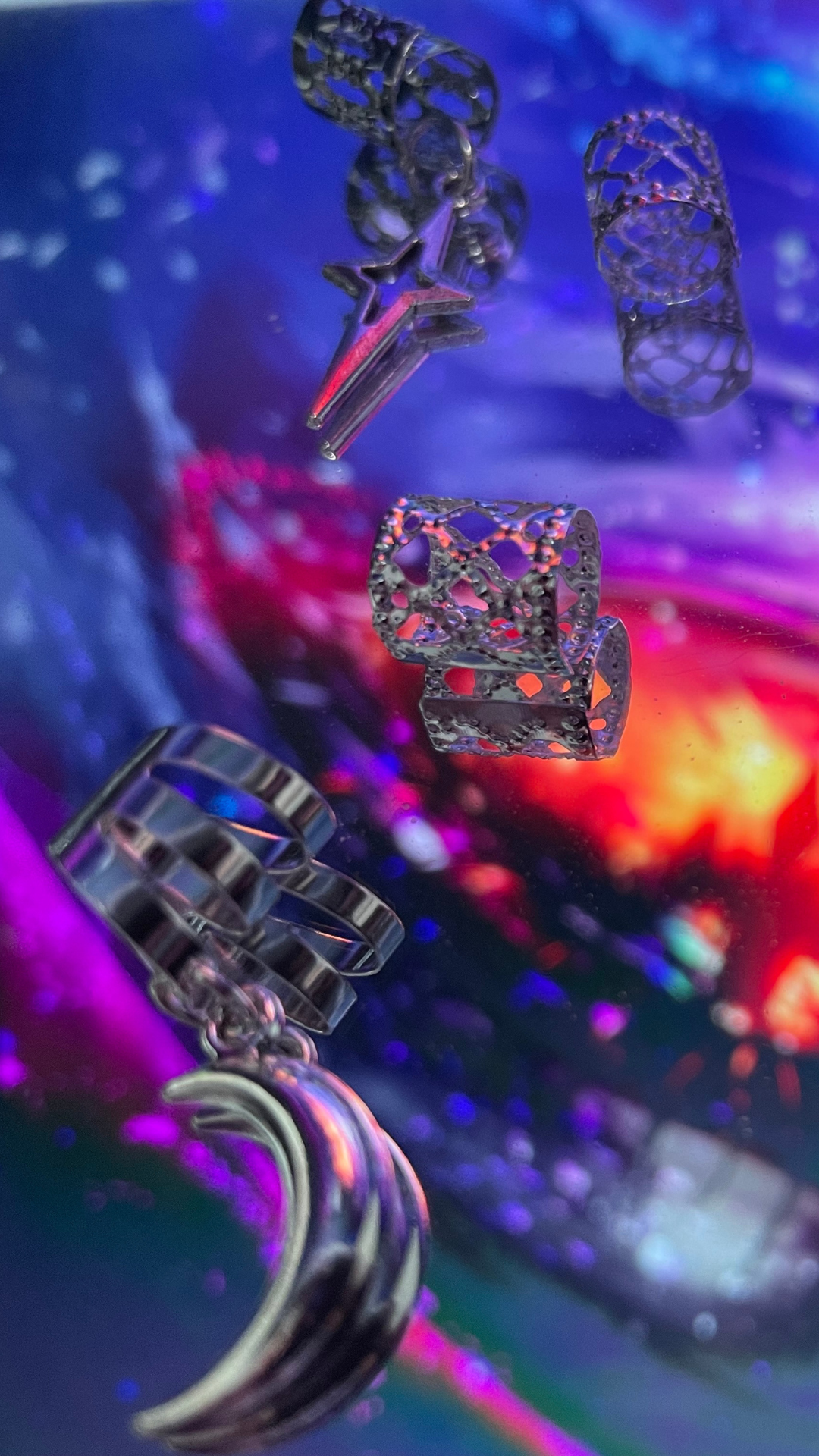 Close-up of various metallic jewelry pieces, including rings and ear cuffs, floating against a colorful, abstract background with vibrant purple, pink, and orange hues.