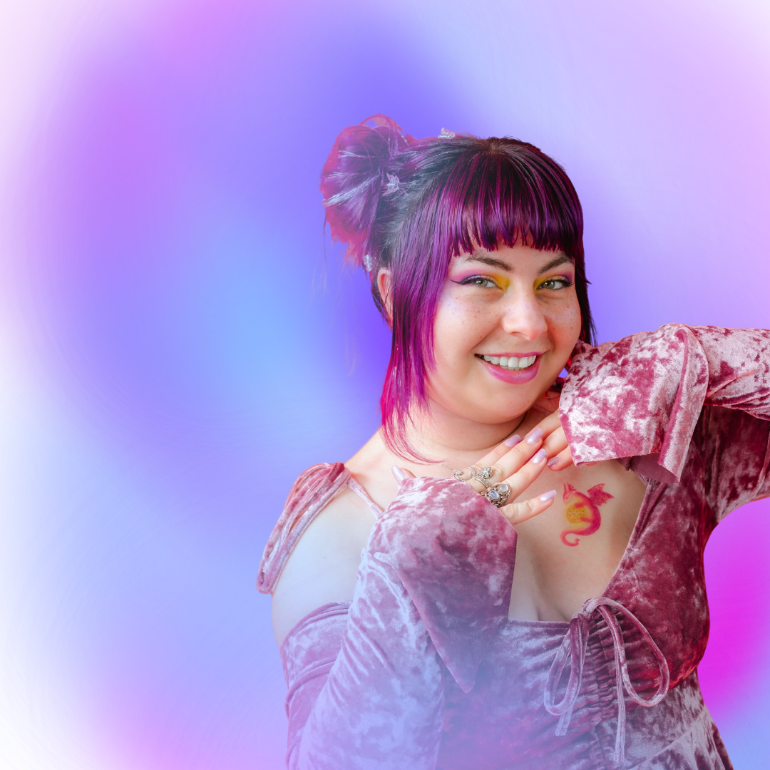 A young woman with purple hair styled in two buns and fringe, wearing a pink velvet off-shoulder top, smiling with her hand near her face, purple and blue background