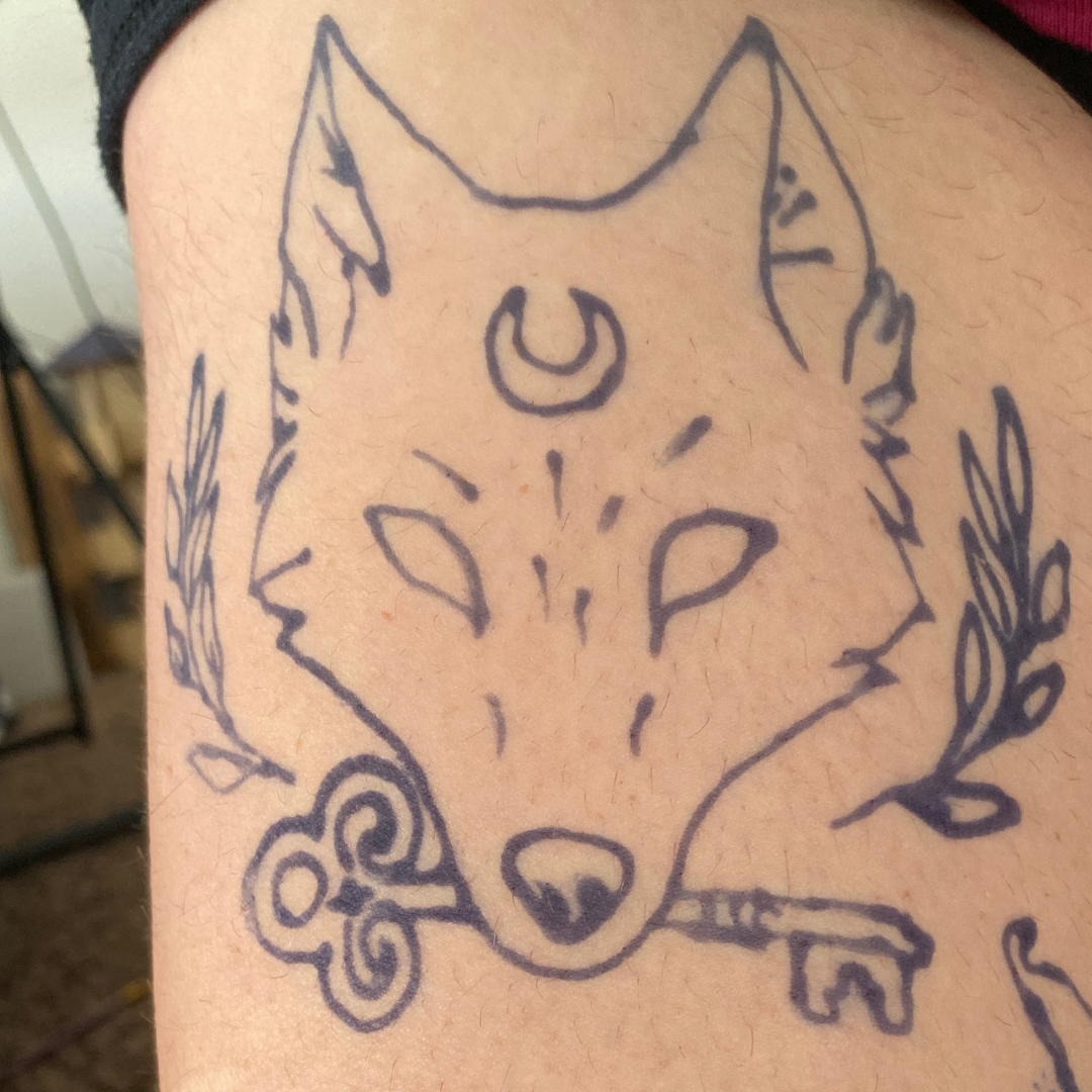 Line drawing of a fox's face with a crescent moon on its forehead, surrounded by decorative elements, ink on skin