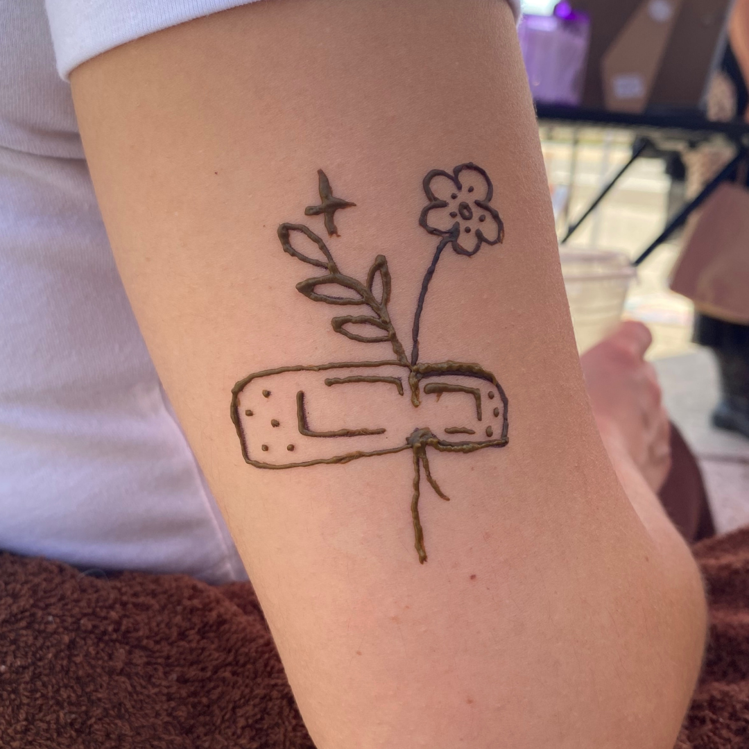 Tattoo of a flower and leaves emerging from a Band-Aid on the person's arm.
