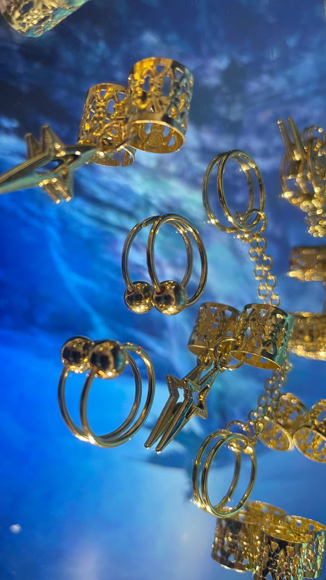 Gold jewelry, including earrings, rings, and chain necklaces, displayed against a blue background.