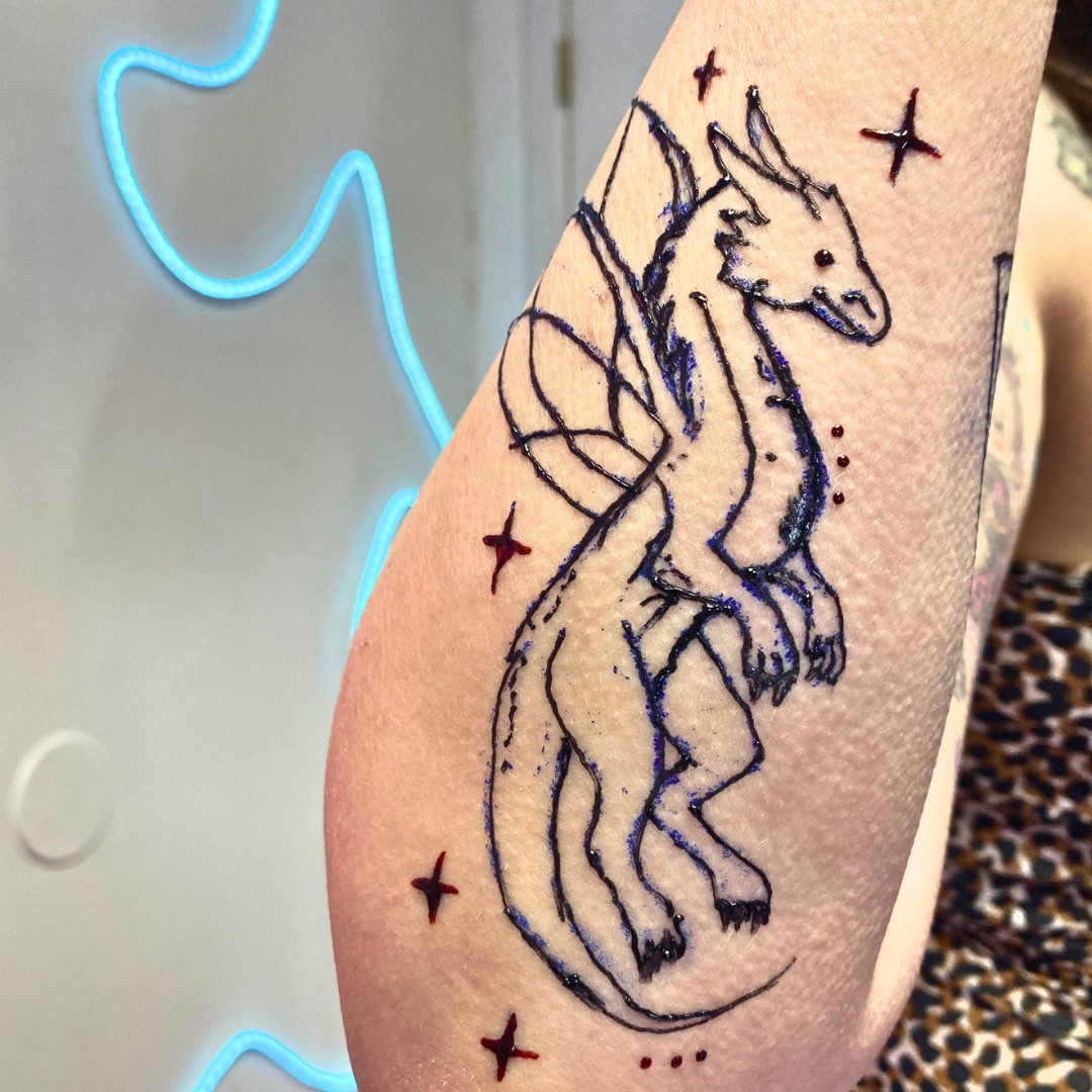 A tattoo of a whimsical unicorn with a flowing mane and tail, surrounded by small red stars, on a person's upper arm.