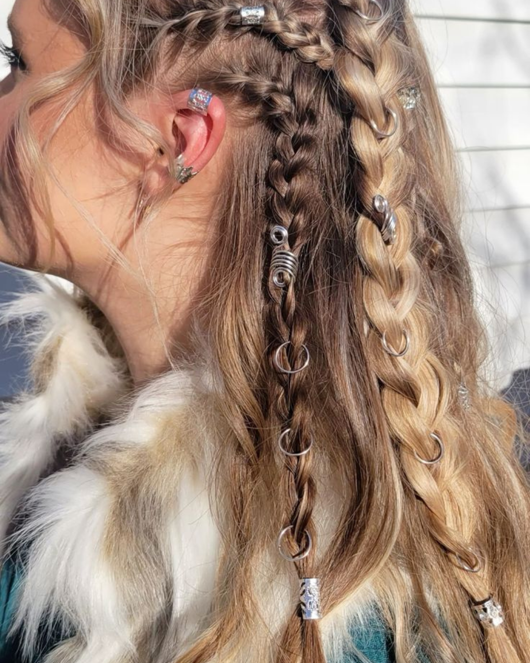 Close-up of a woman's head showcasing her hairstyling with multiple braids and decorated with various metallic hair accessories.