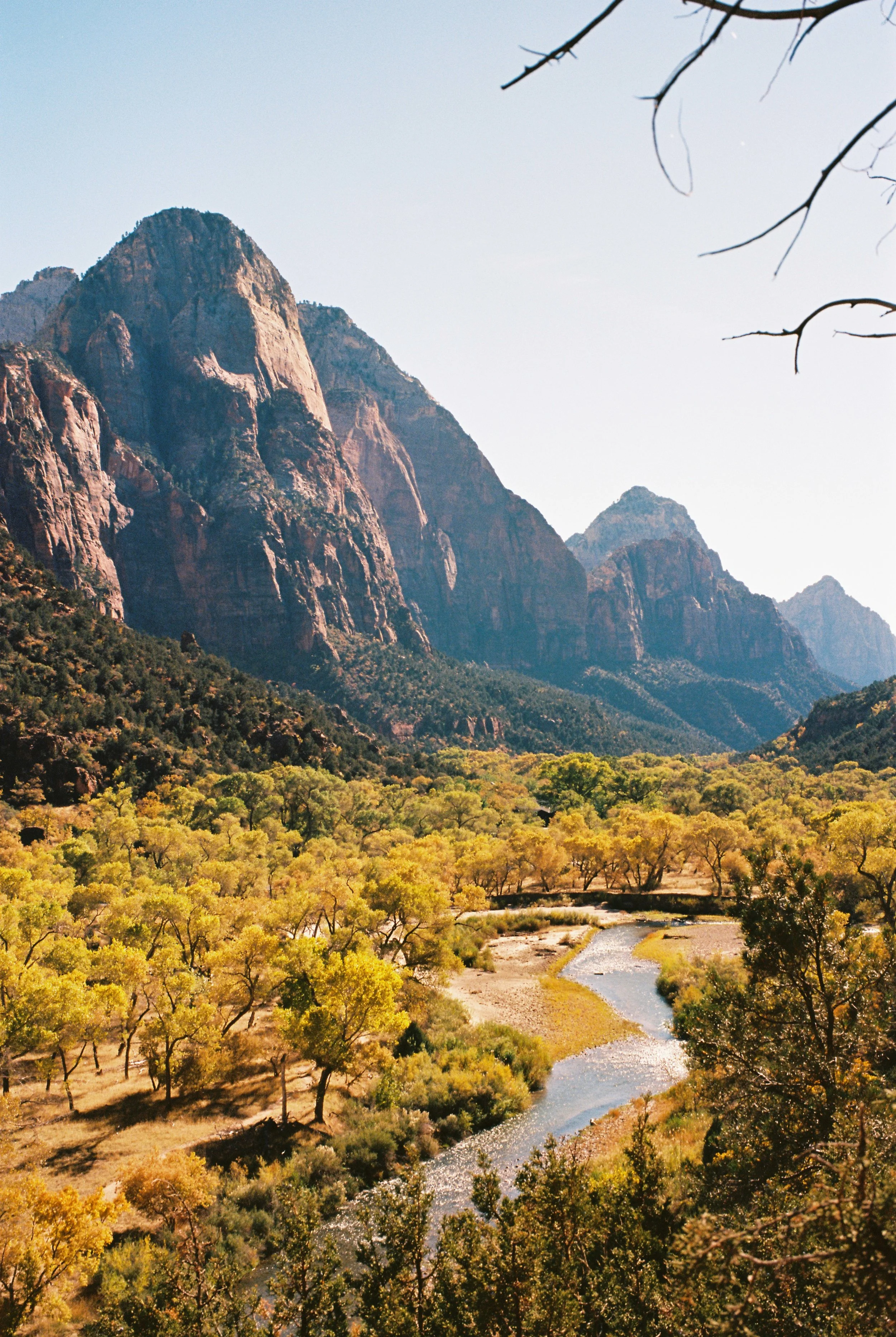 A mountain landscape with rugged peaks, a river flowing through a valley, and trees with autumn foliage in the foreground.