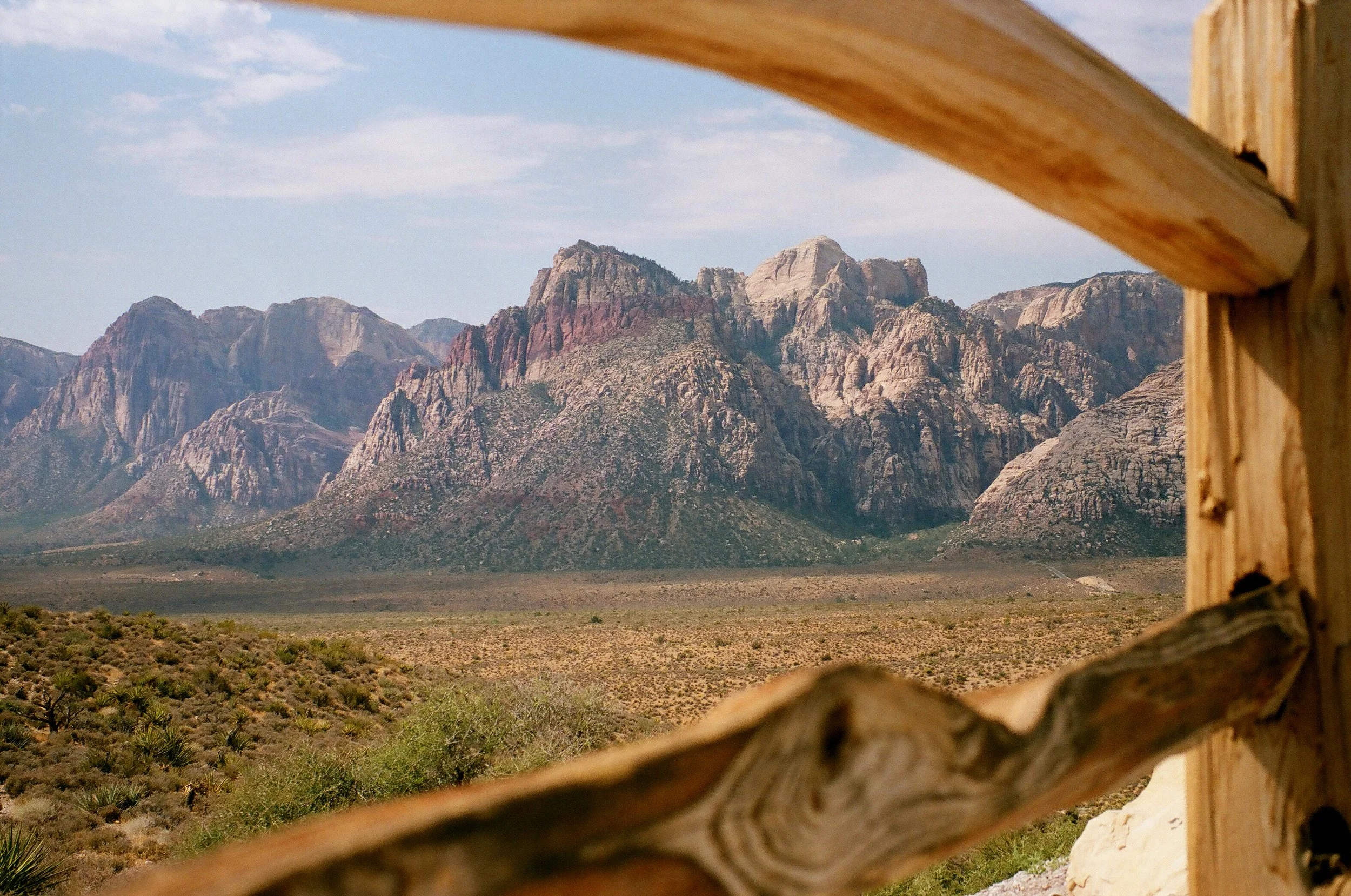 View of rugged mountains in a desert landscape seen through a wooden fence.