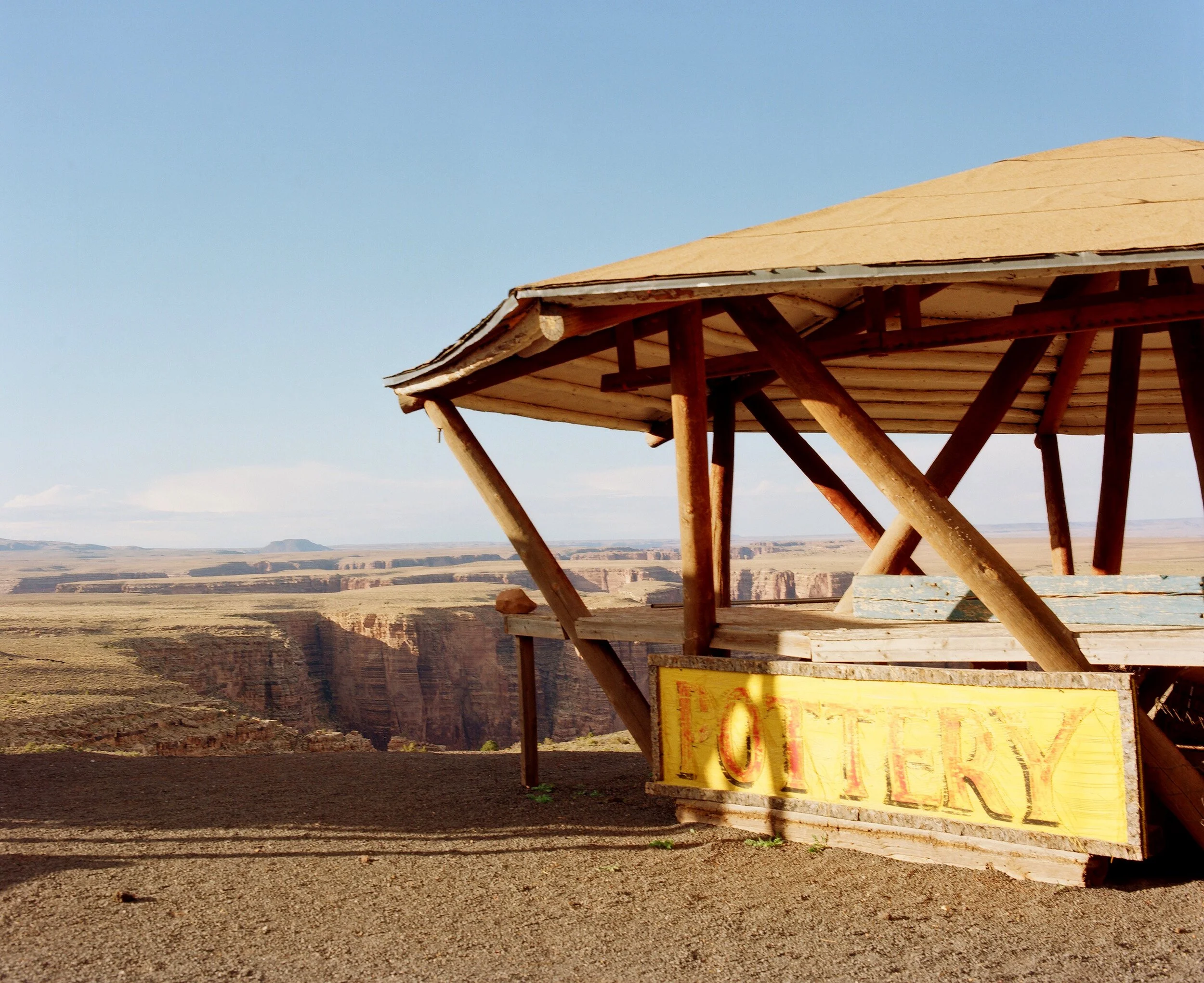 Part of a wooden viewing platform or overlook at the Grand Canyon with a blue sky in the background and a yellow sign attached to the platform.