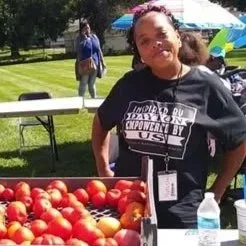 Woman standing next to a display of red tomatoes at outdoor event