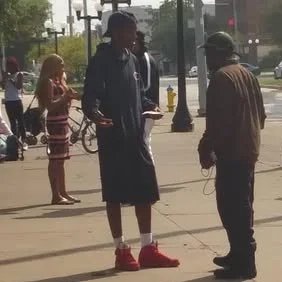 Two men exchanging something on a city sidewalk, with pedestrians and bicycles in the background.