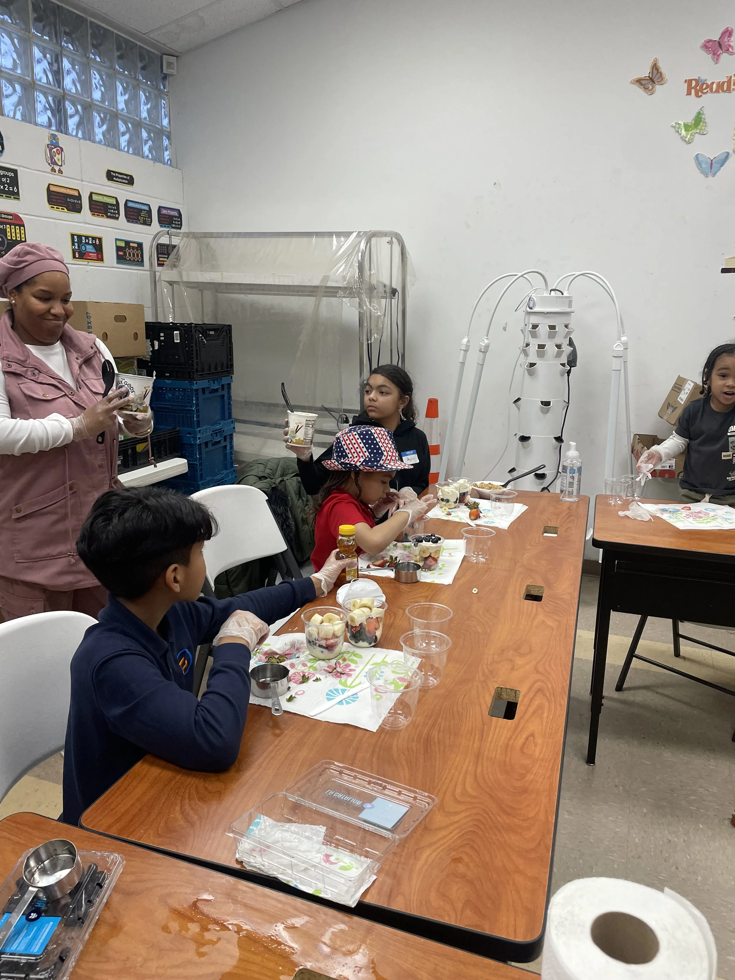Children and adults sitting at a table with dessert cups, celebrating a fun event in a classroom.