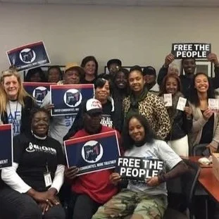 Group of diverse people holding signs that say 'Free the People' and other messages at a meeting or rally.
