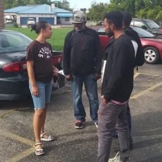 A woman and two men standing and talking in a parking lot.