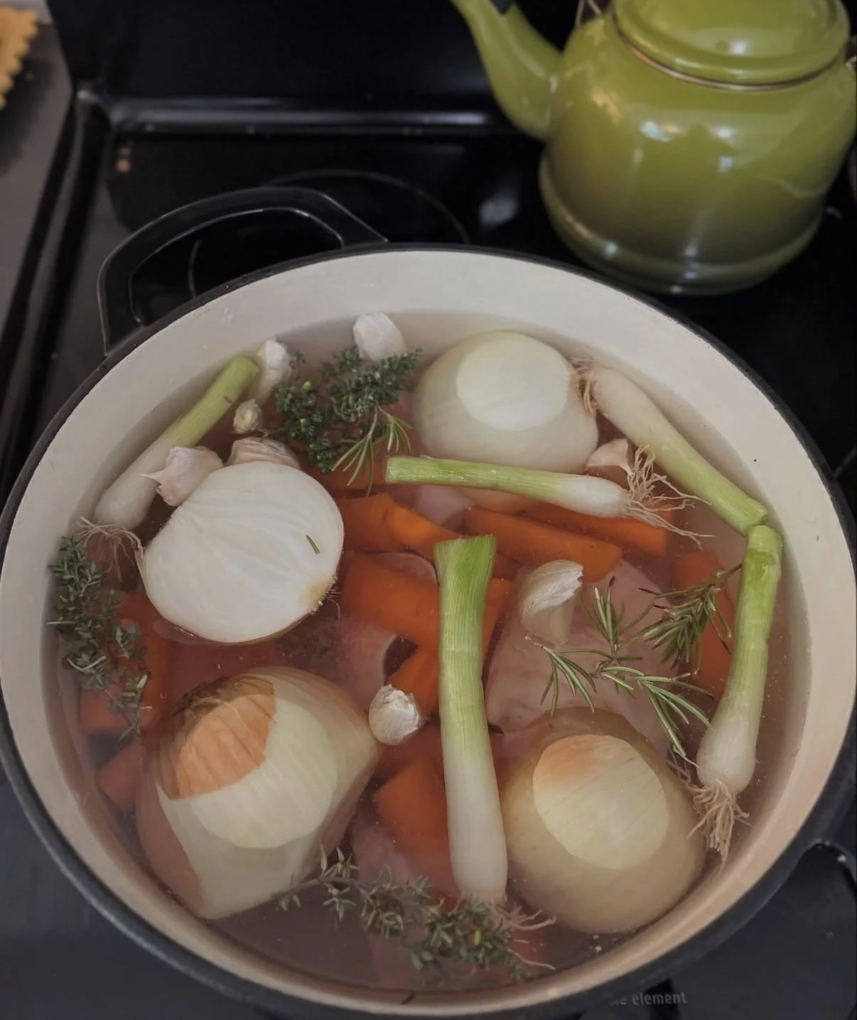 A pot of water with whole onions, carrots, garlic cloves, green onions, and sprigs of thyme submerged for boiling.