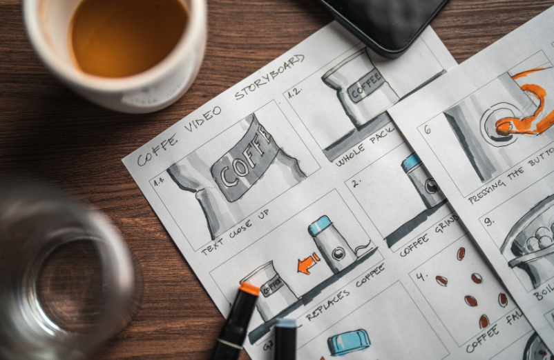 Coffee video storyboard sketches on paper with a coffee cup, a phone, and drawing tools on a wooden table.