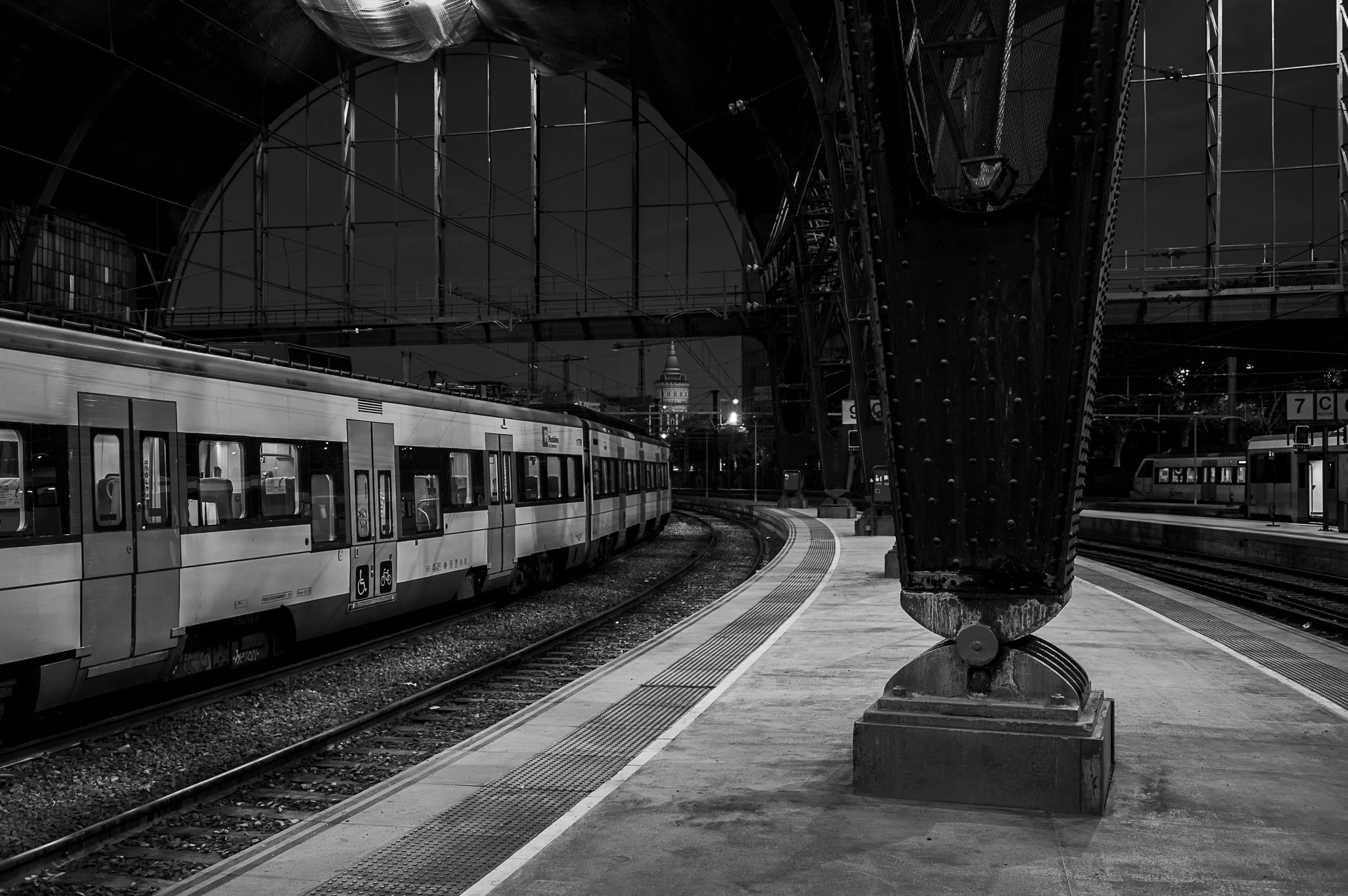 Monumental riveted steel column and curving passenger train inside Estació de França.